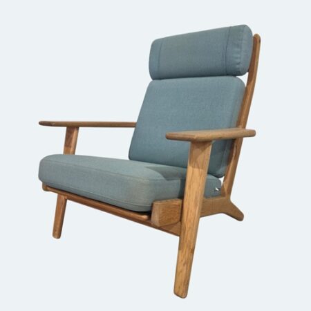 Hans Wegner GE290A high‑back lounge chair by Getama, Denmark, showcasing a solid oak frame, angled legs, broad armrests, and original upholstered cushions in textured fabric