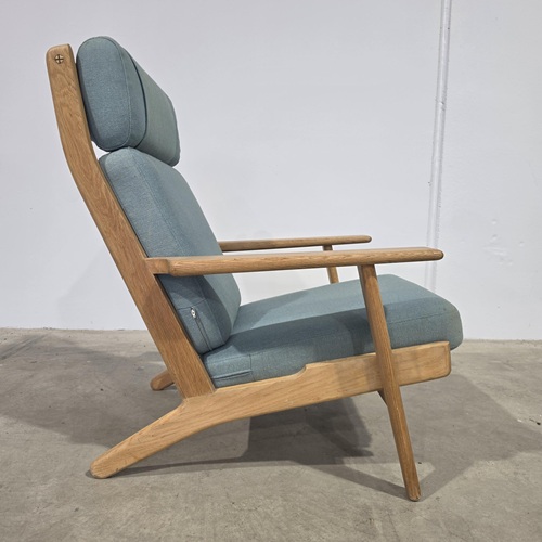 Hans J. Wegner GE290A high‑back lounge chair in solid oak with original textured fabric cushions, featuring sculptural armrests, angled legs, and classic Danish Modern craftsmanship