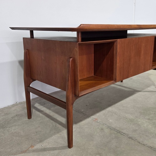 Angled rear‑side view of 1960s Peter Løvig Nielsen teak desk showing teak panel back, tapered legs and sculptural Danish modern silhouette